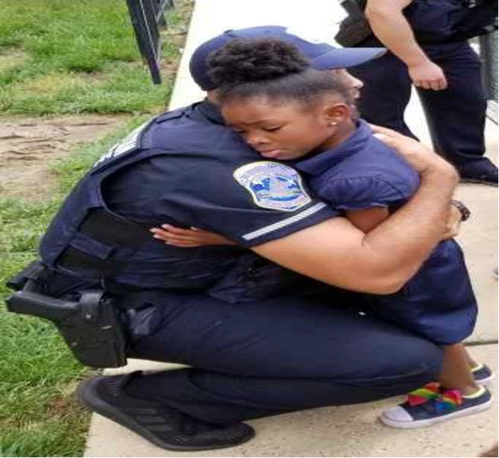Very young black girl embraces a police offer who has squatted down to her level.