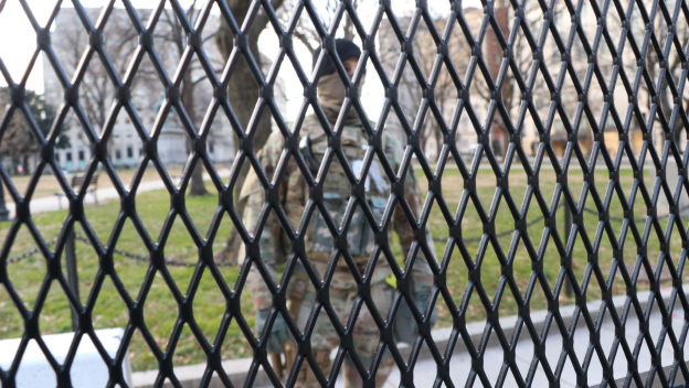 A man in military uniform seen through a fence.