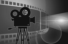 A clipart image of a black movie projector with film behind it.