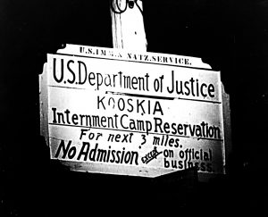 A sign reads "U.S. Department of Justice Kooskia Internment Camp Reservation for Next 3 Miles No admission except on official business