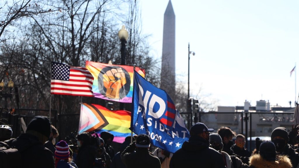Protesters in front of the fence in front of the White House, with gay pride, black power, pro-Biden, and american flags.