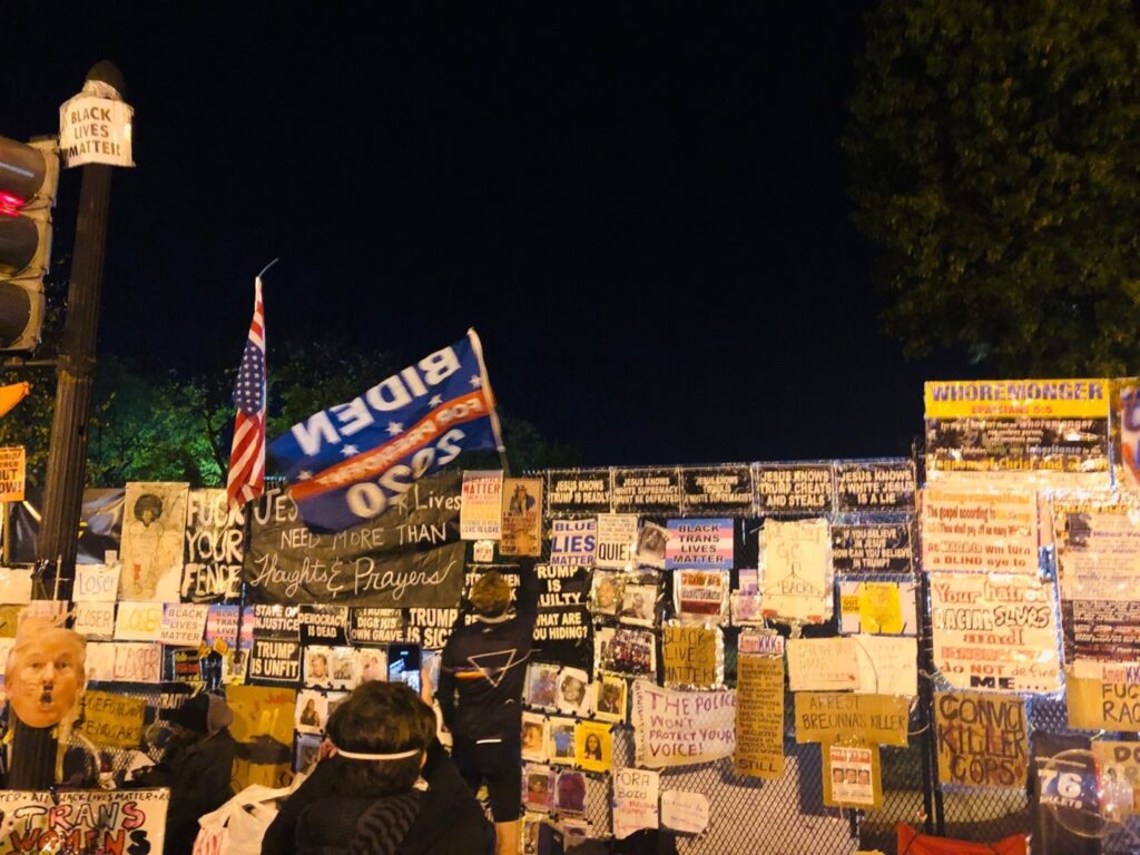 Stretch of White House fence covered in previously described protest signs and art.